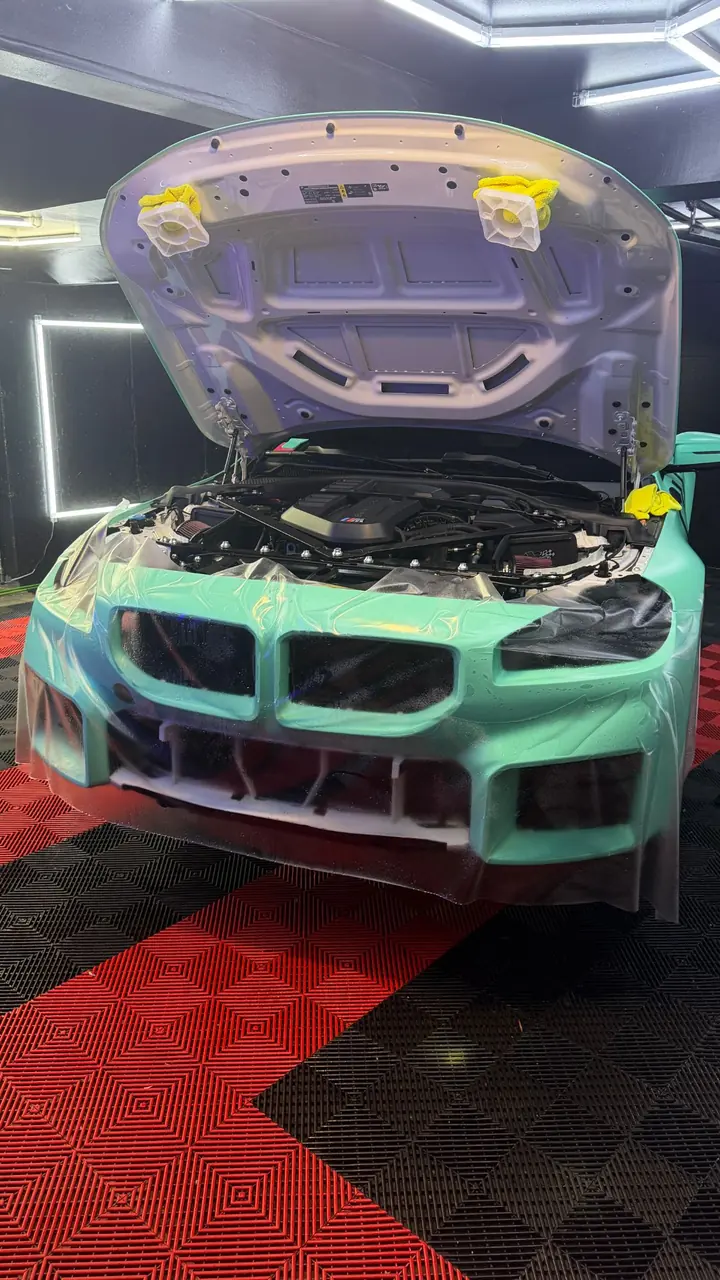 Clear paint protection film being installed on the front bumper of a mint green BMW M2