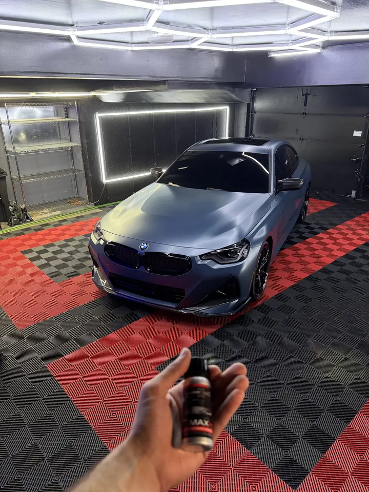 Hand holding a ceramic coating bottle in front of a satin blue BMW M240i